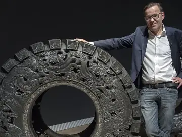 Wim Delvoye pose à côté d'une roue ornée de dragons, une œuvre d'art monumentale.