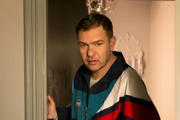 Tomasz Karolak w kolorowej kurtce, jakby wychodził zza drzwi. Może to scena z jednego z jego filmów?