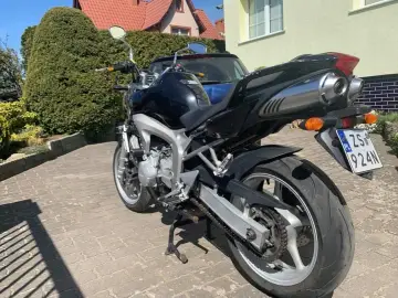 Czarny motocykl Yamaha FZ6 na podjeździe z kostki brukowej, w tle dom i zielone krzewy.