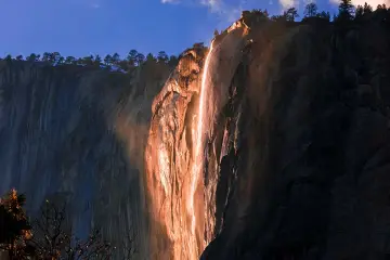 La luz del atardecer ilumina una cascada de fuego en un acantilado rocoso, creando un espectáculo natural.
