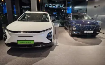 Dwa nowoczesne auta OMODA, białe i granatowe, prezentują się w salonie. To przyszłość motoryzacji, czyli auto hybrydowe.
