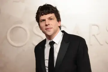 Jesse Eisenberg w czarnym smokingu z czarnym krawatem, na tle napisu OSCARS.
