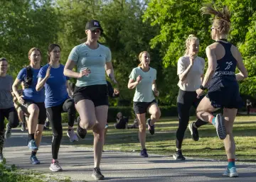 En grupp kvinnor tränar löpning utomhus. De springer i ett parkliknande område, redo att springa 1 km tid.
