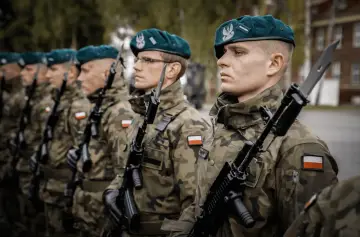 Żołnierze Wojska Polskiego w zielonych beretach i mundurach polowych, z karabinami w rękach, stoją w szeregu.