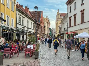 Tłum ludzi spaceruje brukowaną ulicą w Wilnie, siedząc przy stolikach restauracyjnych. Czy wyjazd na Litwę jest bezpieczny? Wygląda na to, że tak!