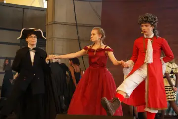 Tancerze w strojach z epoki, w tym wampir w czerwonym płaszczu, biorą udział w musicalu "Taniec wampirów".