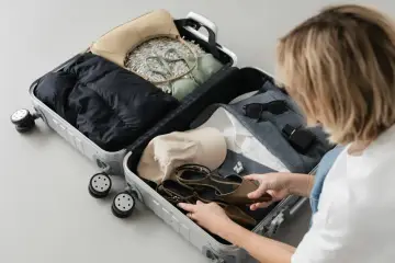 Kobieta pakuje walizkę, układając buty, kurtkę, bieliznę i akcesoria. Gotowa na podróż, z myślą o każdym detalu, by jej enter air bagaż był idealny.