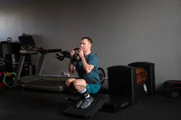 Mężczyzna wykonuje głęboki **squat** z kettlebell w rękach, ćwicząc siłę w siłowni.