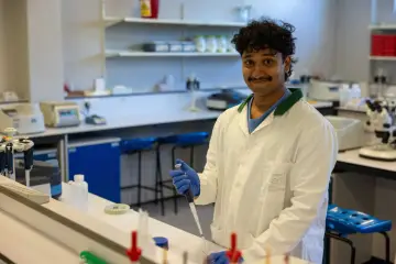 Młody naukowiec w białym fartuchu pracuje w laboratorium, używając pipety. To część jego zbioru zadań biomedica.