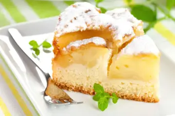 Pyszne, mega szybkie ciasto na oleju z jabłkami, posypane cukrem pudrem, na białym talerzu z miętą i widelcem.