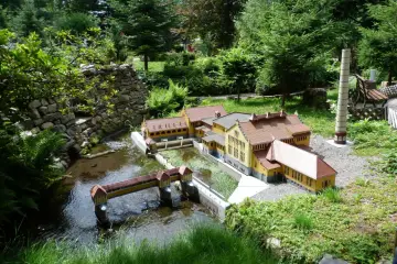 Miniaturowa zabudowa z mostkiem i budynkami, jak w parkach miniatur w Polsce.