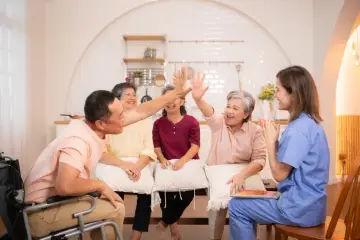 Radosna grupa wsparcia świętuje sukces. Seniorzy i opiekunka śmieją się i klaszczą, czuć pozytywną energię.