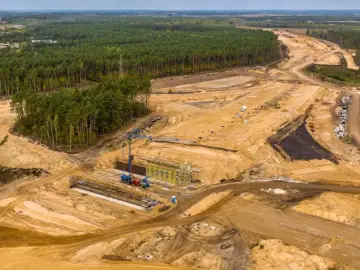 Budowa drogi w lesie, która może być częścią trasy jak dojechać do Sarbinowa. Widoczne koparki, dźwigi i plac budowy.