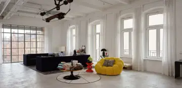 Jasne, oto opis:

Nowoczesny salon w stylu bauhaus z czarną sofą, żółtym fotelem i industrialnymi elementami.