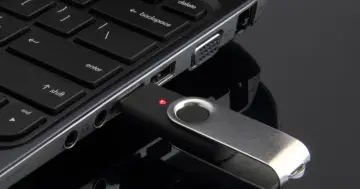 Pendrive podłączony do laptopa, gotowy do kopiowania zdjęć. Czerwona dioda sygnalizuje pracę.