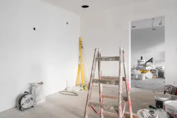 Remont starego domu w toku. Drewniana drabina, poziomice i materiały budowlane czekają na dalsze prace.
