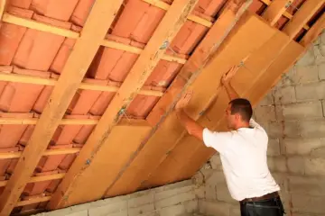 Operaio installa pannelli per la coibentazione del tetto in legno, migliorando l'isolamento termico.