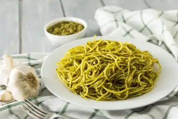 Pyszny makaron z pesto, podany na białym talerzu, obok czosnku i miseczki z sosem.