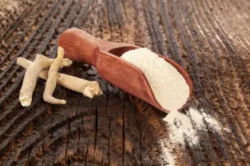 Korzeń ashwagandhy i jej proszek na drewnianym tle. Czy ashwagandha jest szkodliwa? Zazwyczaj nie, ale warto skonsultować się z lekarzem.