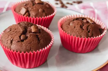 Drei saftige Schokomuffins mit Schokostückchen in roten Papierförmchen, perfekt für Kinder.