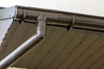 Brązowa rynna z odpływem, widoczny jest jej spadek na rynnie, który zapewnia prawidłowe odprowadzanie wody deszczowej.