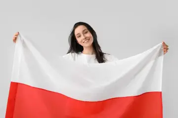 Uśmiechnięta kobieta trzyma polską flagę. Czy 3 maja jest dniem wolnym od pracy? Tak, to święto narodowe!