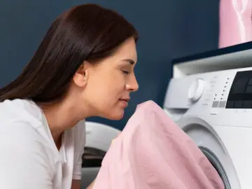 Kobieta wącha różowy materiał, szukając prawdziwych powodów dla których pranie śmierdzi stęchlizną po wyjęciu z bębna.