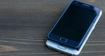 Dwa smartfony leżą na drewnianym blacie. Jeden, ciemny, spoczywa na drugim, srebrnym. Chciałbym skopiować moje urządzenie.