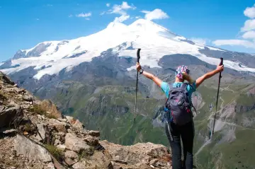 Turystka z plecakiem i kijkami trekkingowymi podziwia najwyższy szczyt Rosji, Elbrus, pokryty śniegiem.