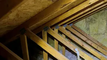 Drewniana konstrukcja dachu z widoczną izolacją. Widać krokwie i przestrzeń między murłatą a dachem, gdzie znajduje się wełna mineralna.