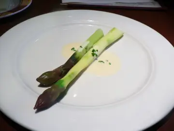Zwei Spargelstangen auf einem Teller, serviert mit einer cremigen beurre blanc Sauce und gehackten Kräutern.