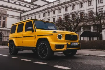 Żółty Mercedes G63 z czarnymi felgami na tle eleganckiego budynku.