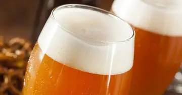 Dwa kufle piwa z obfitą pianką, obok miska precli. Pamiętaj o skutkach picia piwa z kukurydzą lub ryżem w składzie.