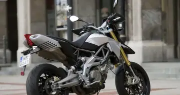 Srebrno-czarny motocykl Aprilia Dorsoduro 750 z żółtymi lagami, gotowy do jazdy po miejskich ulicach.