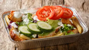 Kapsalon co to? Danie z kurczakiem, frytkami, sałatą, pomidorami i ogórkiem w aluminiowym opakowaniu.