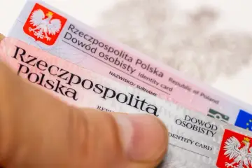 Dłoń trzyma polskie dowody osobiste, gotowe do wymiany. Widoczny orzeł i flagi UE.