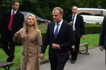 Donald Tusk i jego żona idą trzymając się za ręce, otoczeni przez ochronę.