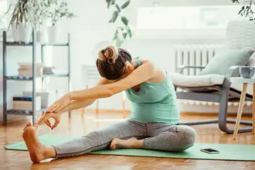 Kobieta wykonuje ćwiczenia **stretching co to** jest, siedząc na macie w domu.