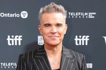 Robbie Williams, znany również jako aktor, w stylowej marynarce w paski na tle logo TIFF.