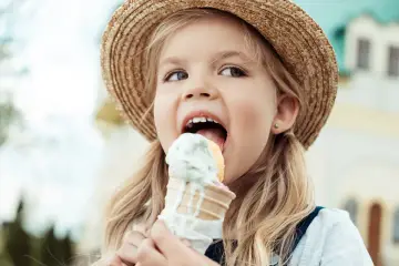 Mała dziewczynka w słomkowym kapeluszu zajada lody na patyku, które mogą pomóc na anginę.
