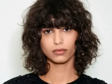 Kobieta z burzą ciemnych, kręconych włosów w stylu bob. Jej loki tworzą naturalną, swobodną fryzurę.