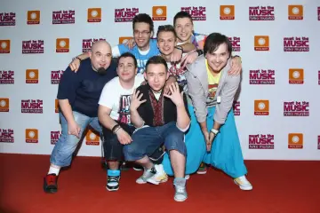 Siedmiu uśmiechniętych mężczyzn pozuje do zdjęcia. Wszyscy enej członkowie zespołu są w dobrych humorach.