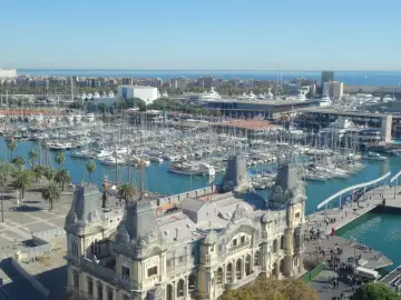 Widok na port pełen jachtów i statków, z charakterystycznym budynkiem w stylu barokowym na pierwszym planie. Tak właśnie wygląda Barcelona.