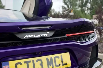Fioletowy McLaren GT z otwartymi drzwiami, widok na tył z logo i tablicą rejestracyjną.