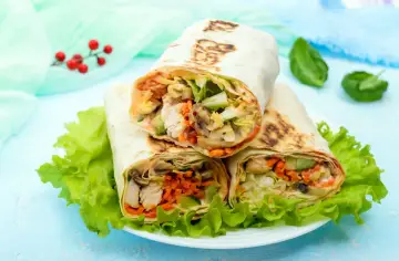 Trzy sycące shoarma drobiowa z kurczakiem, warzywami i grzybami, podane na liściach sałaty.