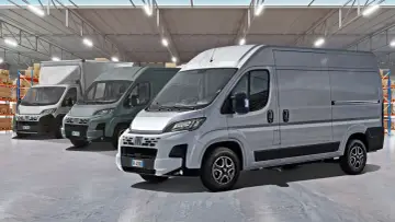 Rząd szarych furgonetek Fiat Ducato Maxi w magazynie z półkami i pudełkami.