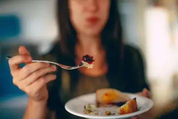 Kobieta bierze widelcem kęs ciasta z dżemem, co może symbolizować nieumiarkowanie w jedzeniu i piciu.