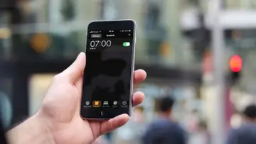 Dłoń trzyma iPhone'a z włączonym budzikiem na godzinę 07:00.