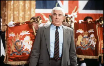 Leslie Nielsen w filmach, serialach i programach zawsze potrafił rozbawić. Tutaj w scenie z królewskimi sztandarami i trąbkami.