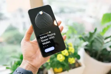Dłoń trzyma iPhone'a z aplikacją Wallet, która ułatwia płatności. Technologia NFC w iPhone'ie sprawia, że transakcje są szybkie i bezpieczne.